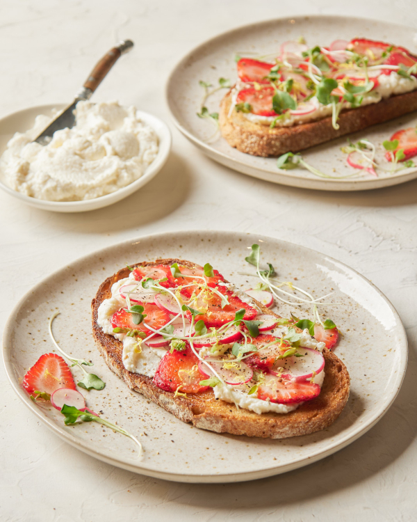 Deux tranches de pain grillé garnies de ricotta fouettée à la cassonade, de fraises et de radis tranchés, ainsi que de micro-pousses, présentées avec un bol de ricotta fouettée à la cassonade