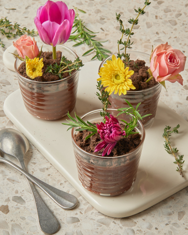 Trois portions de pudding au chocolat saupoudré de miettes de biscuits et garni de fleurs comestibles.