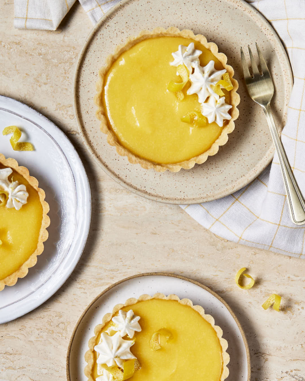 Trois tartelettes au lemon curd garnies de crème fouettée et de zeste de citron sont présentées sur un comptoir en marbre.