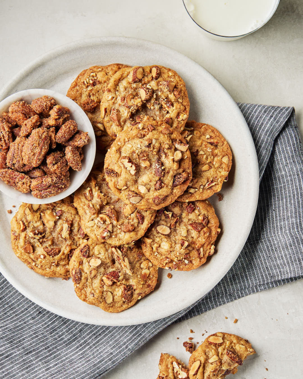 Une assiette de biscuits faits maison avec des noix sucrées et épicées hachées, un bol de noix confites entières et un verre de lait. 