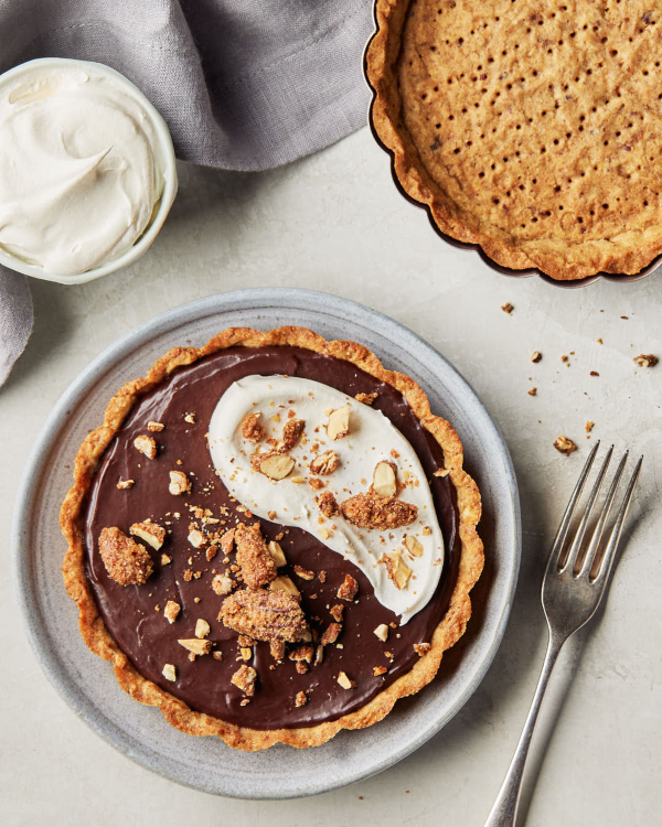 Une pointe de tarte au chocolat en croûte sucrée aux noix, garnie de noix sucrées et épicées, et une croûte vide dans un moule.