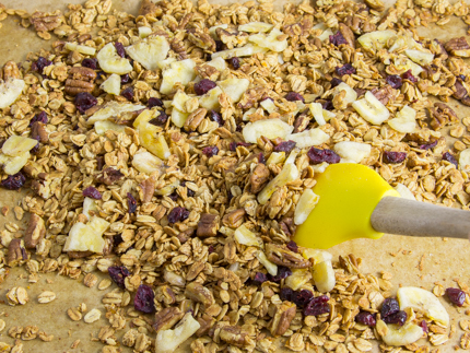 Les bananes et canneberges séchées se faisant mélanger au granola sur une plaque à pâtisserie tapissée de papier parchemin