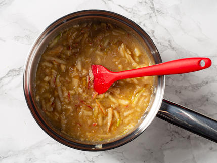 Pommes râpées et ingrédients liquides dans une casserole avec une cuillère à remuer