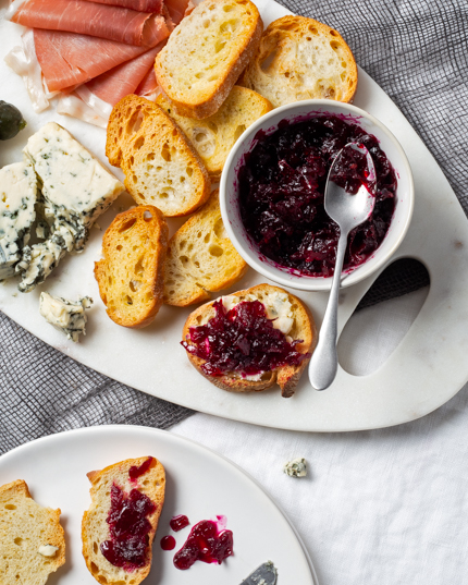 Un plat de confiture de betterave et d’oignon rouge épicée sur un plateau garni de fromages, de charcuteries et de crostini