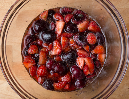 Un bol à mélanger en verre rempli de fraises coupées et de cerises dans un liquide.