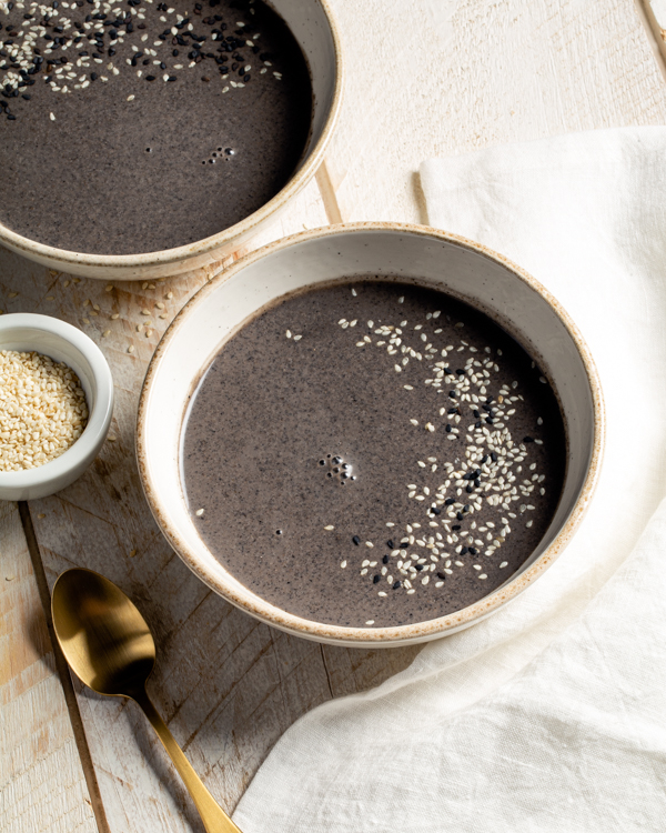 Trois bols de soupe au sésame noir avec une garniture de graines de sésame blanches et noires, placés sur une table en bois