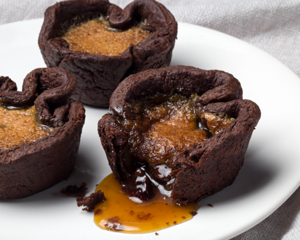 Tartelettes au beurre chocolatées disposées sur une assiette, dont une avec sa garniture qui coule