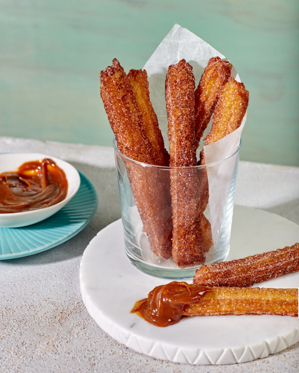 Churros au sucre de cannelle servis dans un verre avec un bol de dulce de leche