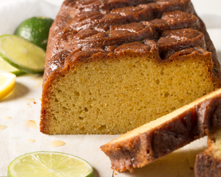 Un gâteau quatre-quarts tranché à une extrémité, disposé sur une assiette décorée de tranches de citron et de lime