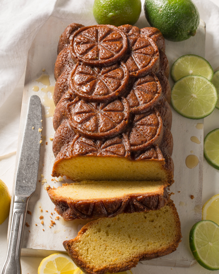 Un gâteau quatre-quarts tranché à une extrémité, disposé sur une assiette décorée de tranches de citron et de lime