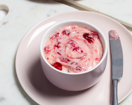 Un bol rose de fromage à la crème aux canneberges rôties, sur une assiette et avec un couteau