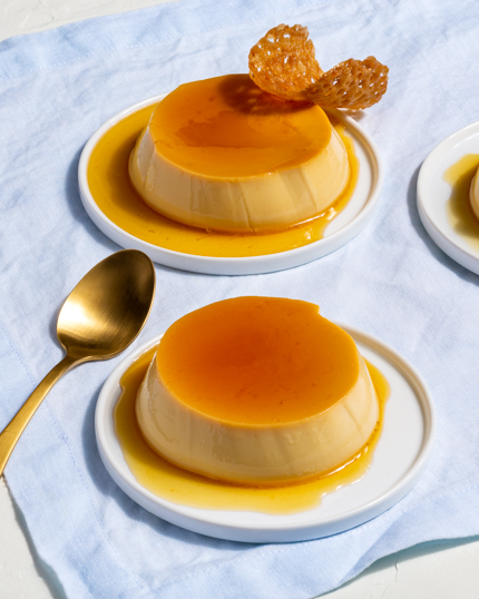 Deux crème caramels garnis de tuiles servies sur des assiettes avec cuillère