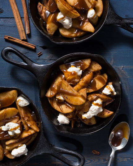 Trois poêles en fonte de poutine dessert incluant les tranches de pommes, la sauce au caramel et le fromage à la crème sucré