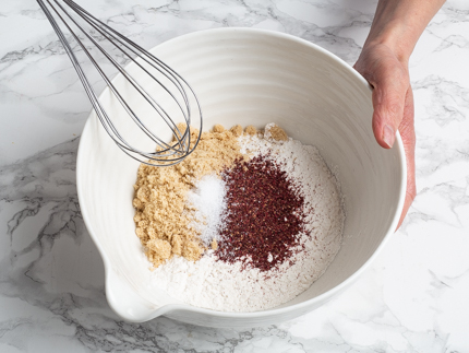 Un bol de farine, sucre, sel et hibiscus avec un fouet 