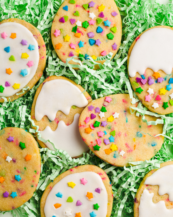 Biscuits en forme d’œufs de Pâques décorés avec des confettis et du glaçage royal, disposés dans un nid fait de rubans verts comestibles