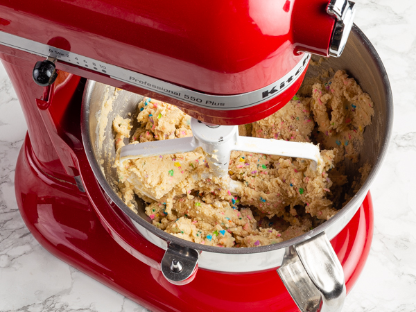 Pâte à biscuits avec confettis dans le bol d’un batteur sur socle