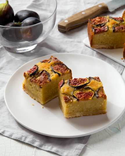 Carrés figues et amandes dans une assiette, un bol de figues à l’arrière