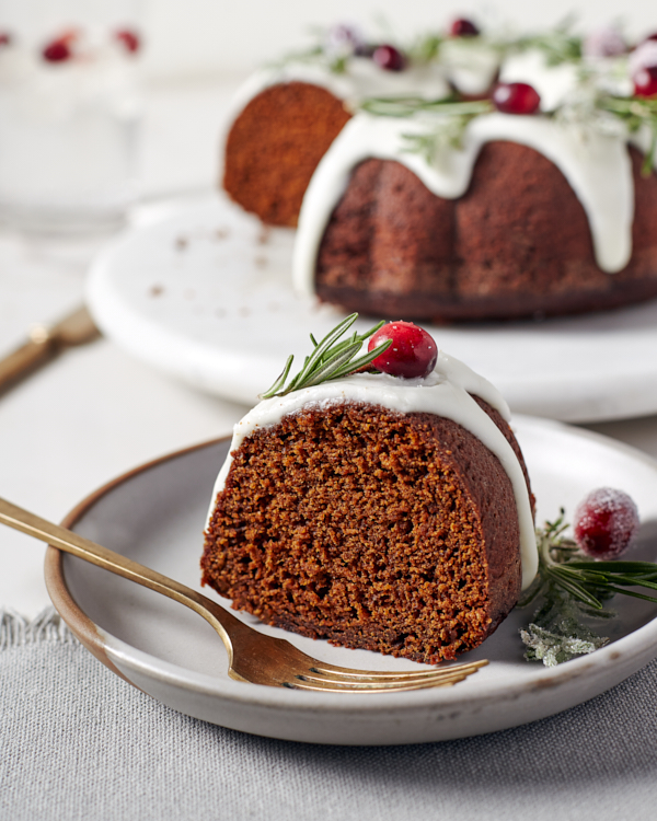 Un morceau de gâteau Bundt au pain d’épices glacé sur une assiette garnie de canneberges et de branches de romarin