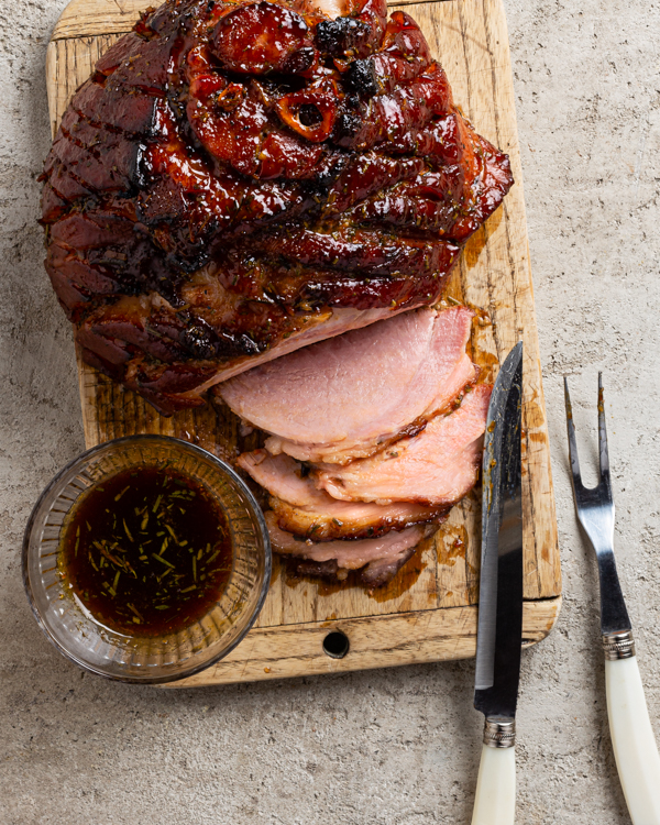 Vue de dessus d'un jambon glacé rôti sur une planche à découper avec un couteau et une fourchette à découper avec plusieurs tranches