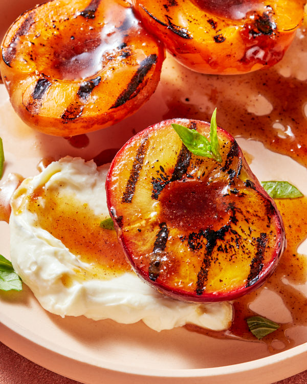 Trois moitiés de pêches grillées avec une garniture de mascarpone et de basilic, et un filet de glaçure à la cassonade sur une assiette