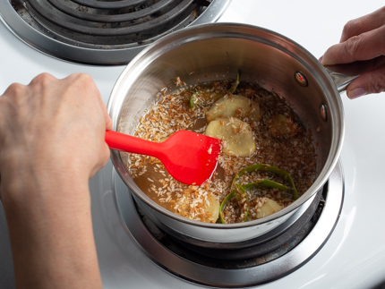 Avec une cuillère en plastique rouge, mélanger dans une casserole la noix de coco, les tranches de gingembre, les zestes de lime et le jus de lime