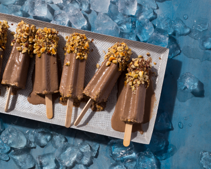 Sucettes de kulfi au chocolat avec des noisettes hachées, fondant dans un plateau