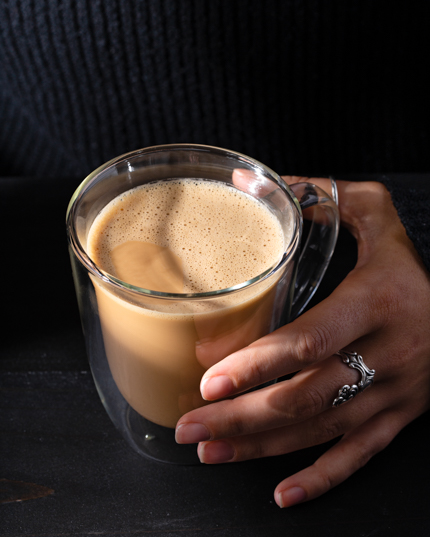 La main d’une femme tenant une tasse en verre remplie de kopi cham sur une table noire