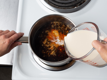 Verser le lait évaporé à partir d’une tasse à mesurer en verre dans une casserole avec de l’eau chaude et des feuilles de thé