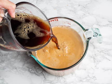 Verser le café à partir d’une tasse à mesurer en verre dans le mélange de thé avec lait évaporé