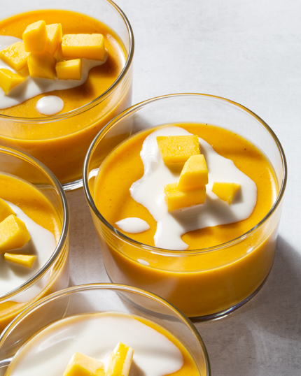 Quatre bols de verre de pouding à la mangue garni de mangue et de lait évaporé