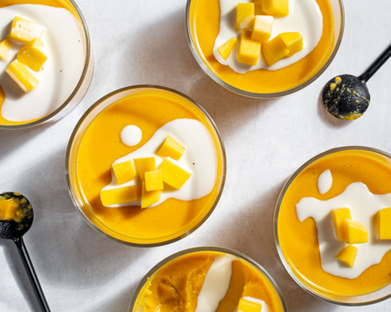 Cinq bols de verre de pouding à la mangue garni de mangue et de lait évaporé, et deux cuillères noires