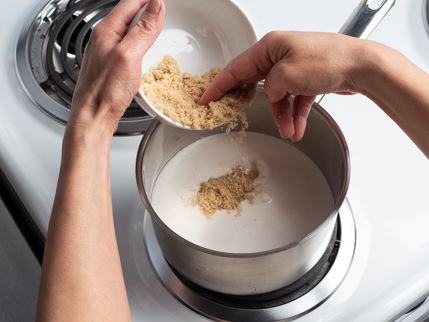 Cassonade Dorée Redpath qui tombe d’un bol dans une casserole de lait de coco sur une cuisinière