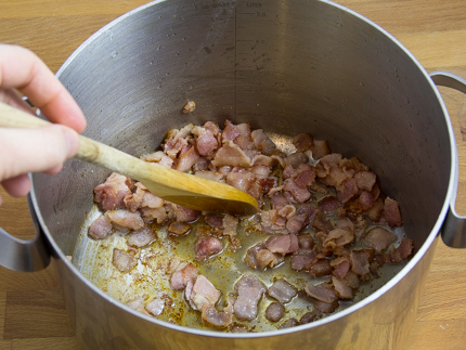 Casserole avec du bacon haché se faisant remuer avec une cuillère de bois