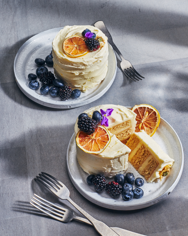 Deux mini-gâteaux au citron et à la camomille sur des assiettes, dont une avec une tranche coupée, servis avec des baies et garnis de baies