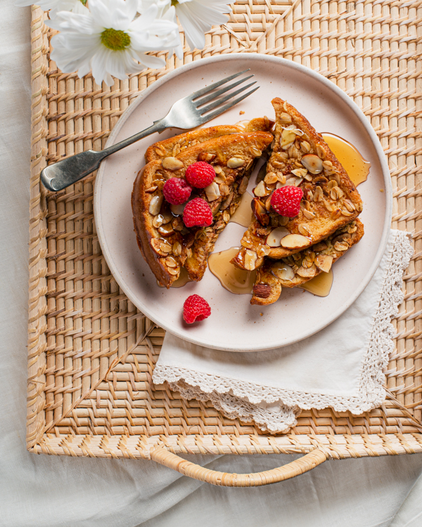 Pain doré croustillant avoine et amandes avec du sirop sur un plateau de service en rotin avec une fourchette et des fleurs