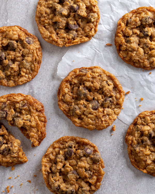 Sept biscuits aux flocons d'avoine et aux pépites de chocolat sur un comptoir avec du papier parchemin, dont un cassé en deux