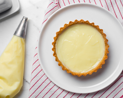 Une poche à douille à côté d'une croûte à tarte garnie de crème