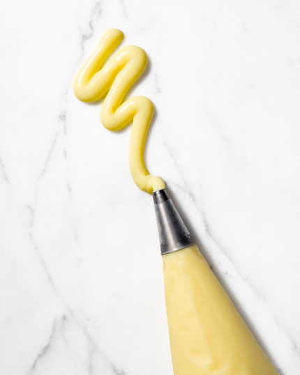 Crème pâtissière sortant d'une poche à douille se faisant déposer sur un plateau de marbre