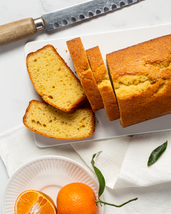 Gâteau quatre-quarts à l’orange sur un plateau avec quatre tranches coupées, un couteau et des oranges