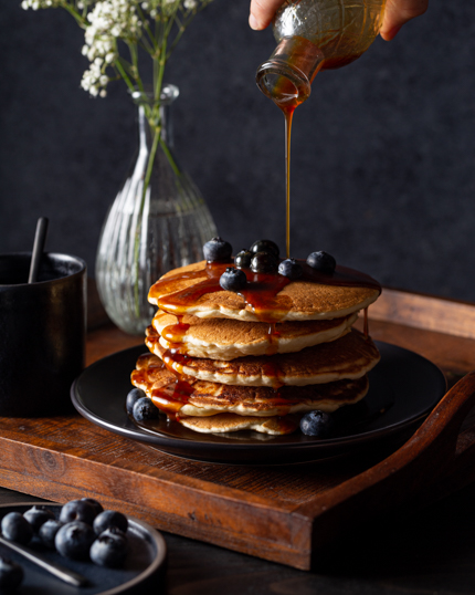 Verser le sirop à la mélasse d’une bouteille sur une pile de pancakes aux bleuets