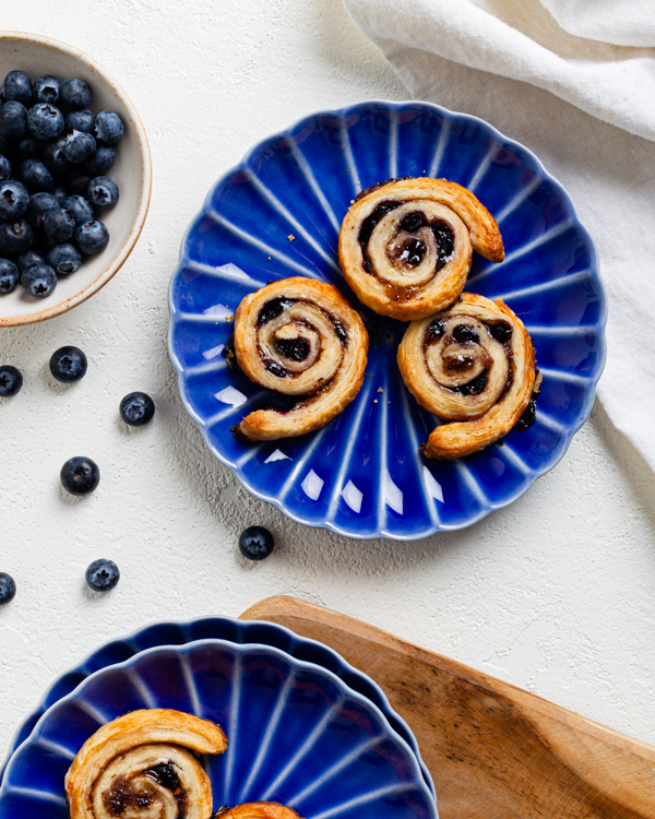 Assiettes bleues avec des pets-de-sœur aux bleuets sur une surface blanche et un bol de bleuets