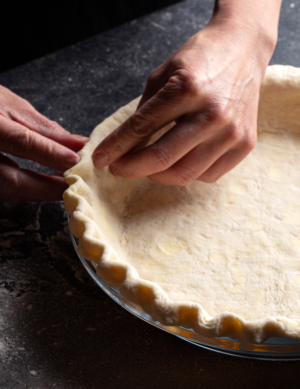 Deux mains qui cannèlent le pourtour d’une pâte