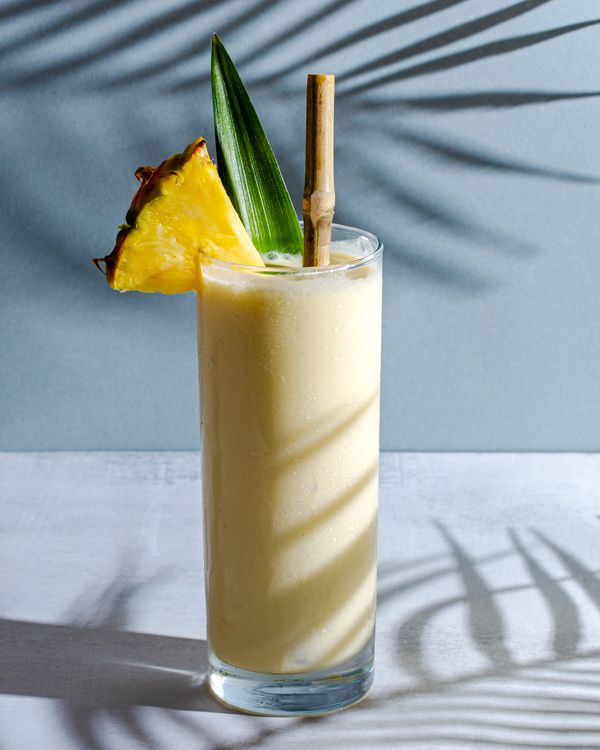 Un verre de pina colada décoré d’un bâtonnet et d’une feuille d’ananas avec une paille en bambou