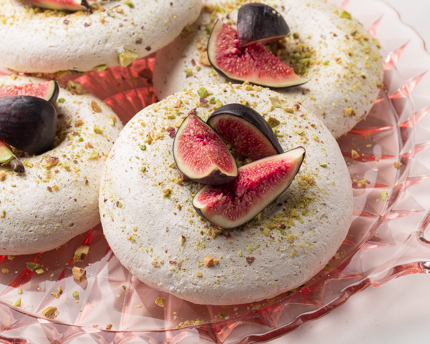 Meringues dans une assiette en verre, garnies de pistaches et de figues