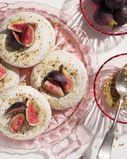 Meringues dans une assiette en verre, garnies de pistaches et de figues