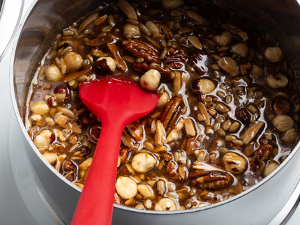 Chaudron rempli du mélange de sucre fondu, de noisettes, de pacanes, d’amandes et de graines de tournesol avec une cuillère en silicone