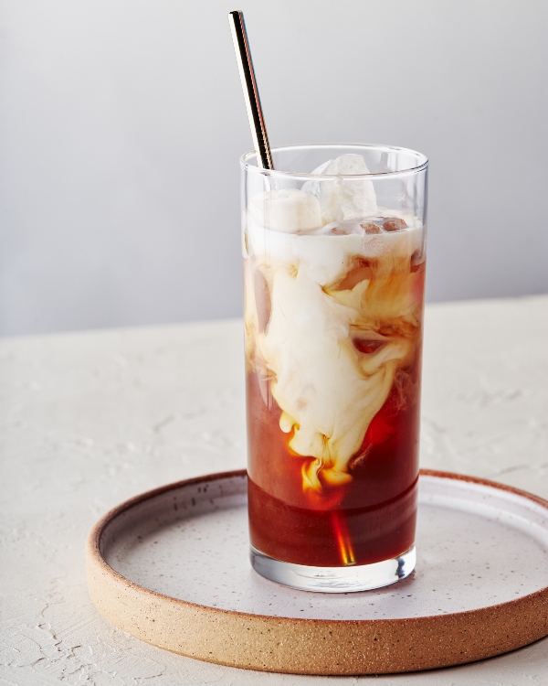 Un verre de cold brew aux épices de citrouille avec crème sur de la glace, servi avec une paille réutilisable.