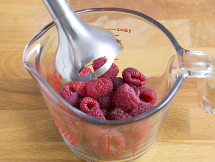 Une tasse à mesurer remplie de framboises prêtes à être réduites en purée