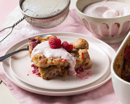 Une assiette présentant une portion de pouding au pain avec de la crème et des framboises