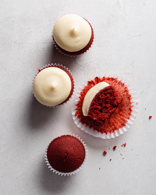 Quatre cupcakes red velvet avec glaçage au fromage à la crème sur un comptoir, un sans glaçage et un coupé en deux